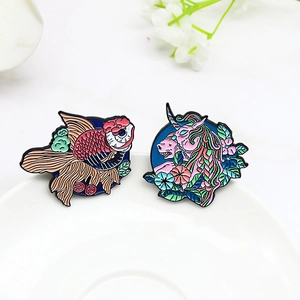 Broches en émail avec poisson rouge et licorne fleurie sur un plateau blanc élégant
