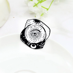 Mystical black and white enamel brooch with sun, moon, and eye on a white ceramic plate