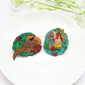Exquisite hand-painted enamel toucan and long-tailed bird brooches on a white ceramic tray