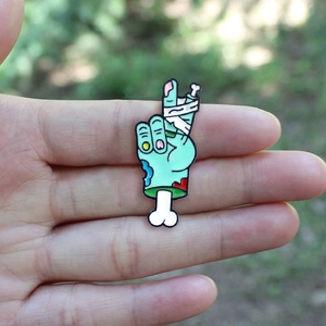 Broche en émail main de squelette zombie avec bandages blancs et geste de la paix