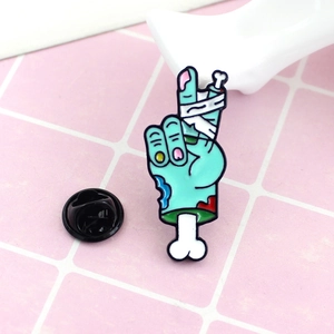 Broche émaillée main de zombie bleue signe V avec bandage et fermoir en caoutchouc
