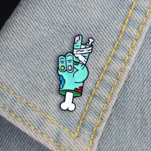 Détail d'un pin's émaillé main de zombie avec bandage sur tissu en denim bleu clair
