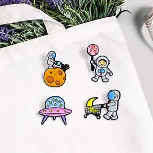 Space astronaut enamel pin set featuring UFO and moon cart on a white canvas bag