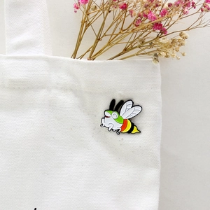 Cartoon bee enamel brooch pin with green and red stripes on a white canvas bag