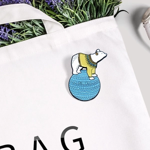 Niedliche Eisbär-Emaille-Brosche auf blauem Ball an einer weißen Stofftasche