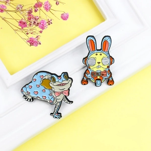 Cartoon robot rabbit and frog enamel pins displayed with elegant decorative dried flowers