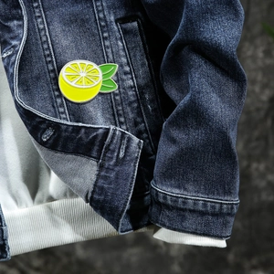 Vibrant lemon enamel brooch with green leaves on denim jacket pocket, casual style