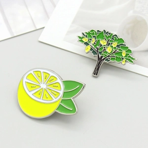 Detailed view of yellow enamel lemon and lemon tree brooch set on a white surface