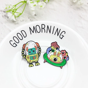 Cartoon space monster and bunny UFO enamel pins set on a white ceramic plate