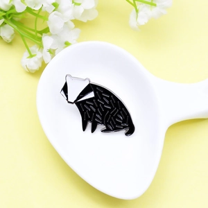 Cute black and white badger enamel brooch pin displayed in a ceramic spoon