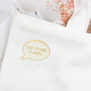 Minimalist speech bubble enamel pin with 'THE FUTURE IS NAPS' text on canvas bag