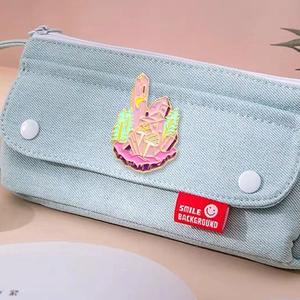 Detail of mushroom and crystal enamel pin attached to a light blue denim bag accessory