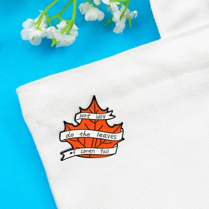 Orange maple leaf enamel brooch with Lorien quote pinned on a white canvas bag