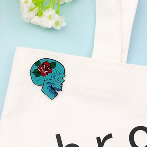 Broche gothique punk avec crâne bleu et rose rouge fixée sur un sac en toile blanc