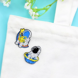 Cartoon astronaut and planet enamel pin set on a white canvas bag with starry decor