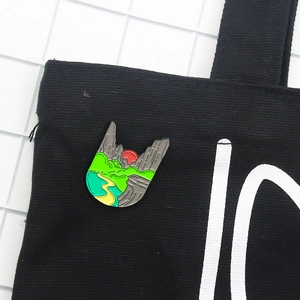 Artistic mountain river landscape enamel brooch featuring a red sunset on black canvas bag