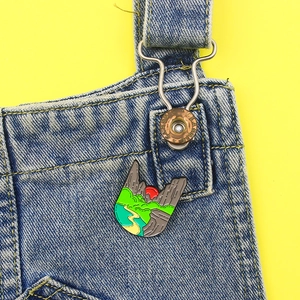 Detail of enamel mountain sunset pin with river and forest scenery on denim jacket