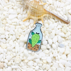 Broche en émail cactus dans une bouteille en verre avec design bleu et détails de terre