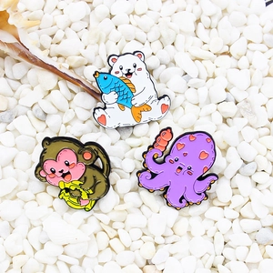 Drei kreative Emaille-Pins mit Eisbär, Affe und Oktopus auf weißen Kieselsteinen