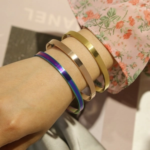 Primo piano di tre braccialetti aperti a C in acciaio inossidabile colorato sul polso.