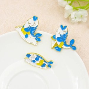 Trois broches en émail de poissons carpes koï colorés sur une assiette en céramique