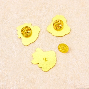 Lot de trois pin's en métal doré avec attaches sur un fond rose texturé