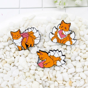 Three-piece cartoon orange fox enamel pins set displayed on white decorative stones