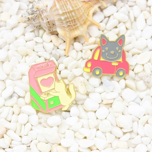 Pins émaillés chat sur console de jeux et chat gris en voiture sur galets blancs