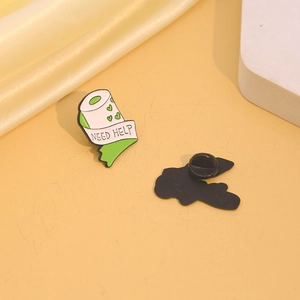 Enamel toilet paper brooch with green heart and Need Help text on yellow silk background