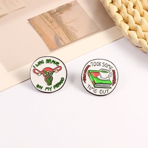 Pair of creative enamel pins featuring floral uterus and cozy book themes on white background