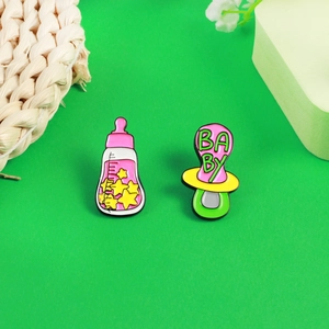 Detail-Set aus rosa Babyflasche und Schnuller Emaille-Anstecknadeln auf Grün