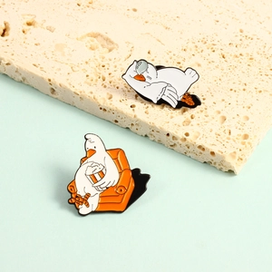 Cute white goose enamel pins featuring a sleeping goose and one eating popcorn on a sofa