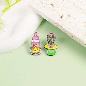 Süßes Emaille-Broschen-Set mit Babyflasche und Schnuller auf grünem Hintergrund
