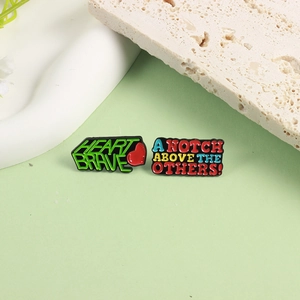 Close-up of enamel pins set with HEART BRAVE text and colorful motivational phrases