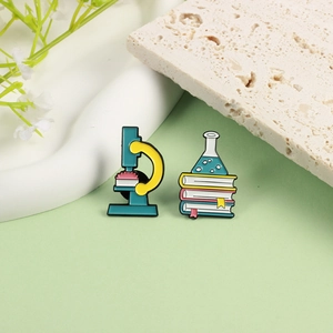 Fashionable science enamel pins featuring a microscope and laboratory flask on books