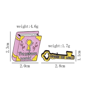 Detailed view of pink book and yellow key enamel pins with size and weight specifications