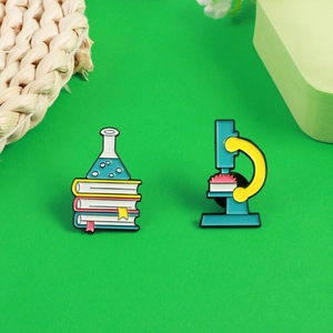 Detail of science enamel pins featuring a microscope and laboratory flask on green background