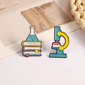 Flat lay of science enamel pins featuring a microscope and laboratory flask on book