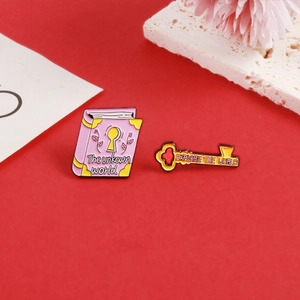 Detail of pink book and gold key enamel pins with motivational quotes for travel