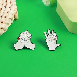 Detailed view of hand-shaped enamel pins with red nails on a green decorative background