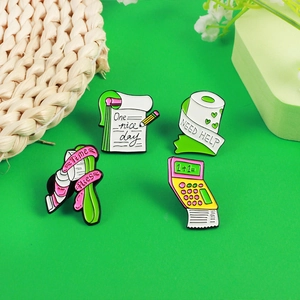 Creative enamel pins featuring calculator, notebook and paper roll designs on a green surface