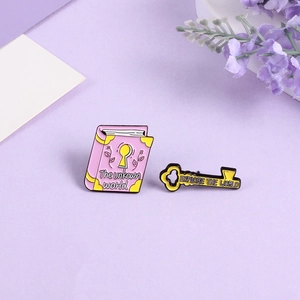 Detail of pink book and yellow key enamel brooch set with EXPLORE THE WORLD text
