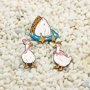 Three cute enamel duck pins with Courage text displayed on clean white pebbles