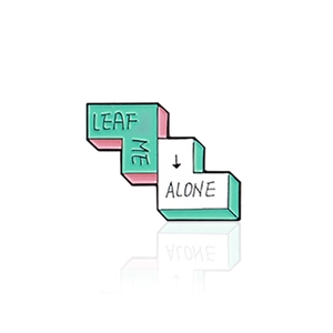 L-shaped enamel pin with Leaf Me Alone slogan in teal and white with reflection