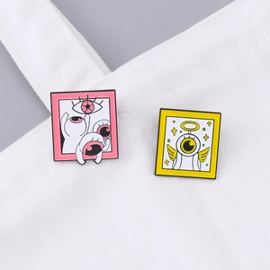 Cartoon enamel pin set with pink eye frame and yellow winged angel on a white canvas bag