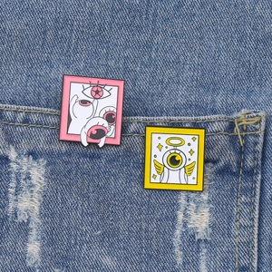 Cartoon enamel pins with pink eye patterns and yellow angel motifs on denim fabric