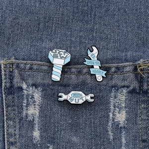 Dreiteiliges Emaille-Anstecknadel-Set mit Industrie-Werkzeugen auf blauem Denim-Hintergrund