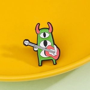 Whimsical green three-eyed monster enamel pin playing guitar on a vibrant yellow base