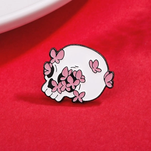 Pink butterfly and white skull enamel brooch pin on textured red fabric background