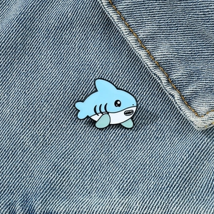 Dettaglio ravvicinato di una spilla a forma di squalo in smalto blu su tessuto denim
